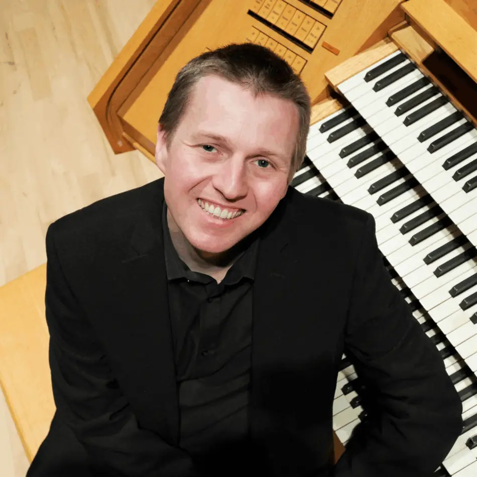 A man looking up at he camera with organ keys behind him
